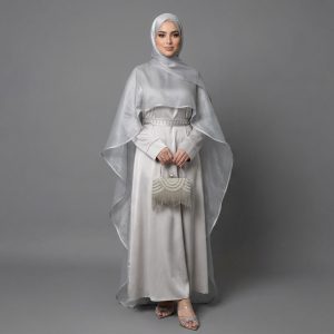 Make a breathtaking entrance with our Cape Abaya, a fusion of contemporary haute couture and traditional modesty. This exquisite piece features a dramatic, sheer shimmering cape that drapes elegantly over a smooth satin inner dress, creating a multi-dimensional look that captures the light from every angle. It’s the ultimate choice for the woman who wants to stand out at high-profile events.